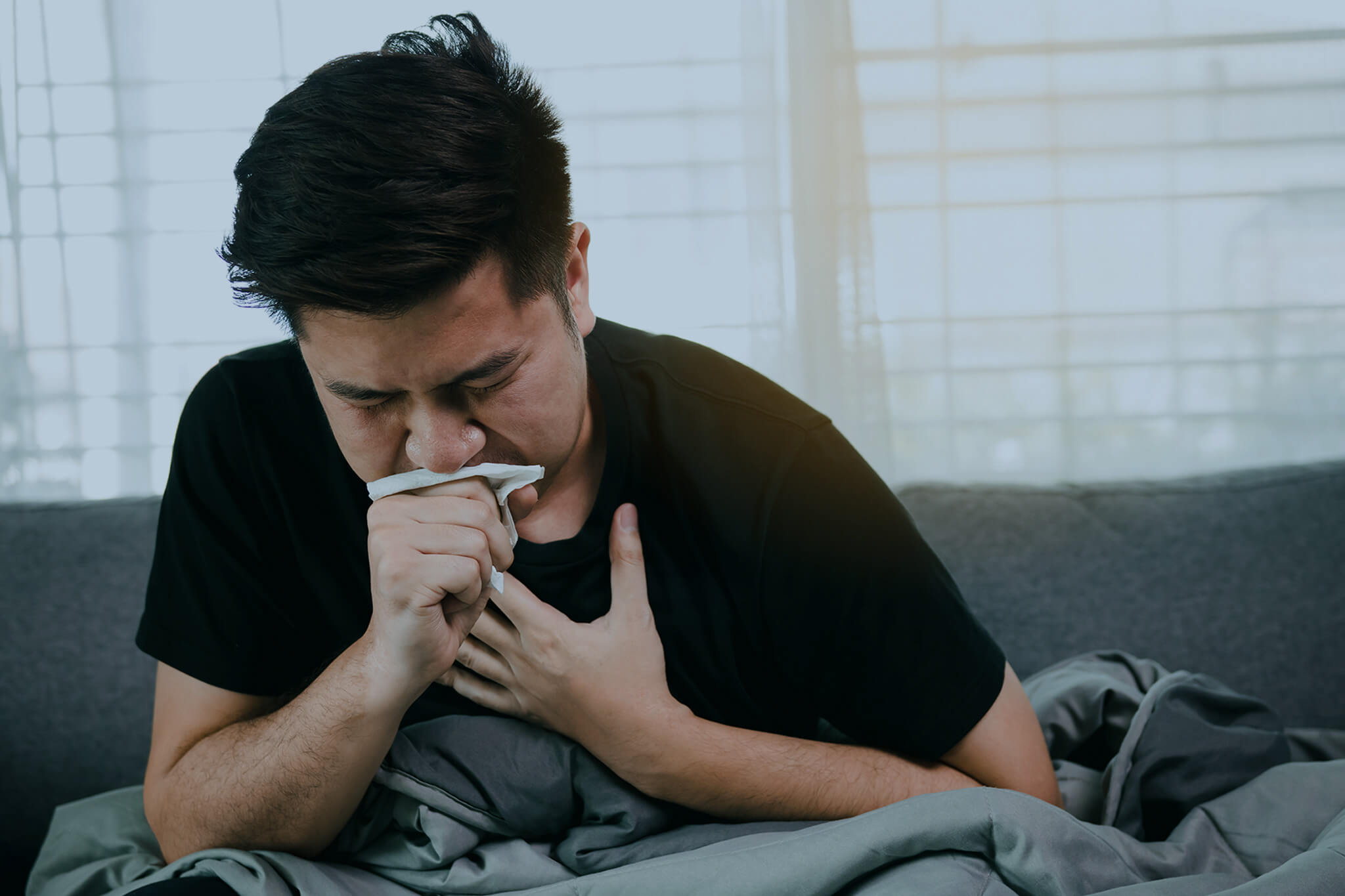 Asian man covering his mouth with tissue paper while coughing.