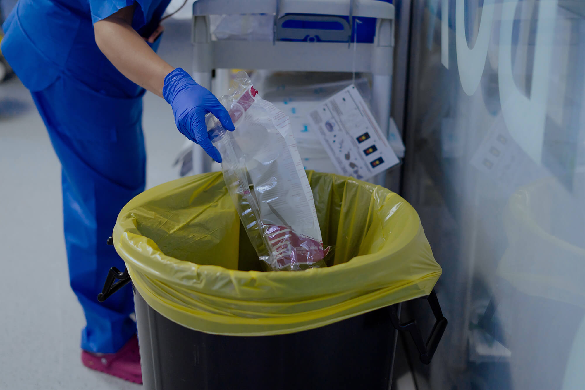 Nurse wearing gloves disposes of medical waste in a designated bin.