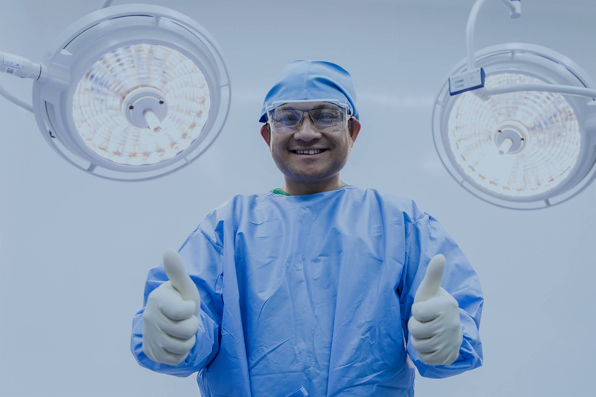 Happy Asian surgeon in blue uniform inside operating room with surgical lamp.