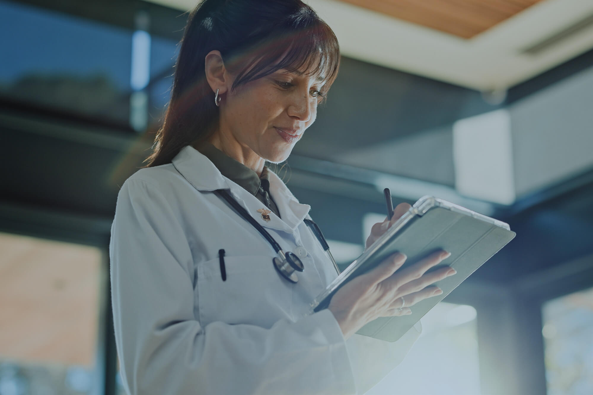 Female doctor in a white lab coat reviewing notes on a tablet.