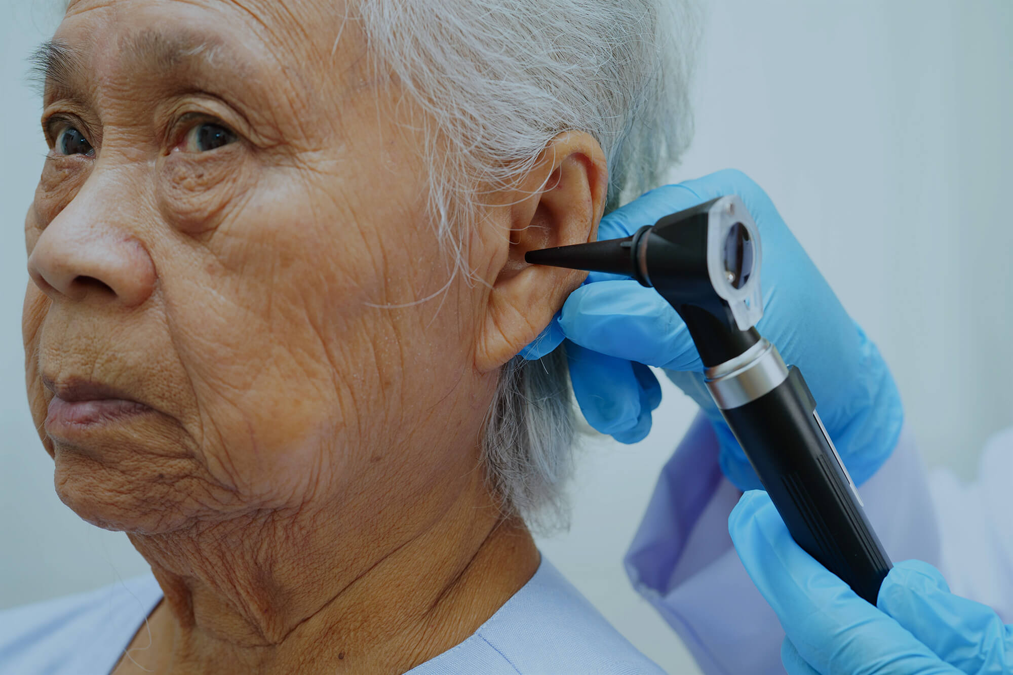 ENT physician doctor examining senior patient ear with otoscope.